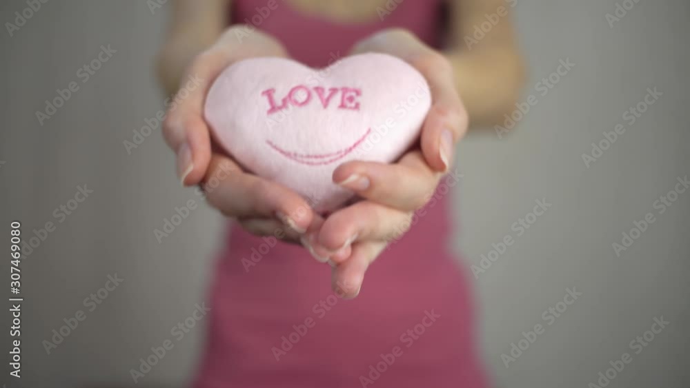 Valentine's Day. Women's hands in defocus hold out a gift in the form of red hearts, like soft toys, to the camera. Valentine's Day. Women's hands in defocus hold out a gift in the form of red hearts, like soft toys, to the camera.