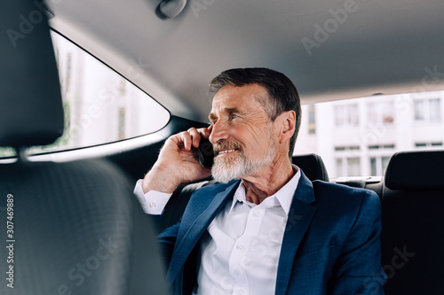 Smiling businessman talking on a cell phone while sitting on a backseat of a taxi © Artem Varnitsin