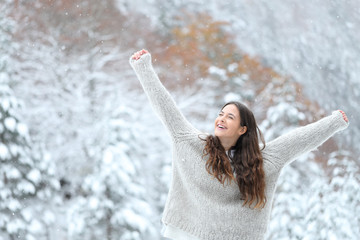 Excited girl enjoying snow in winter raising arms