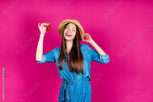 girl summer resident in a straw hat and denim sundress, smiling cheerfully demonstrates strawberries