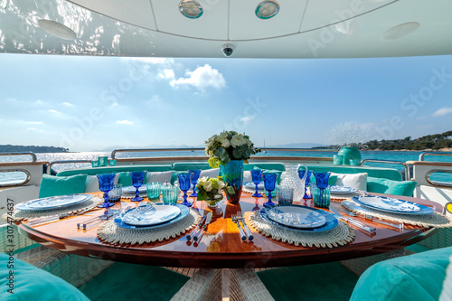Ocean-themed table setting with blue plates, wine glasses and a flower bouquet on a luxury yacht © SPIX PRODUCTION