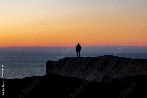 A silhouetted man standing on a cliff looking at the sunset over the ocean