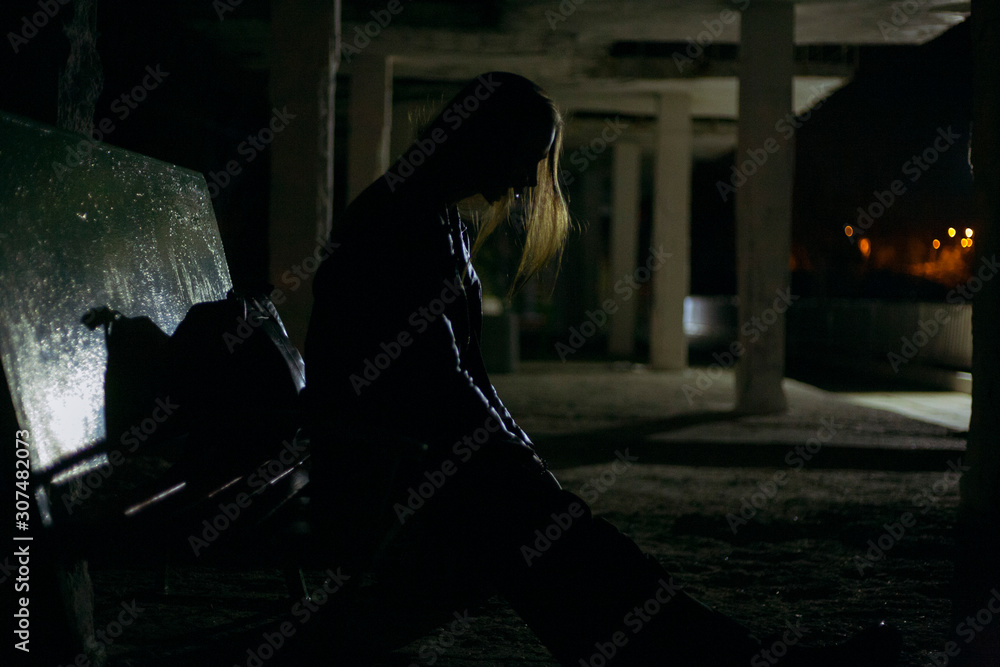 dark silhouette of a sad girl sitting on a bench in a depressive pose ...