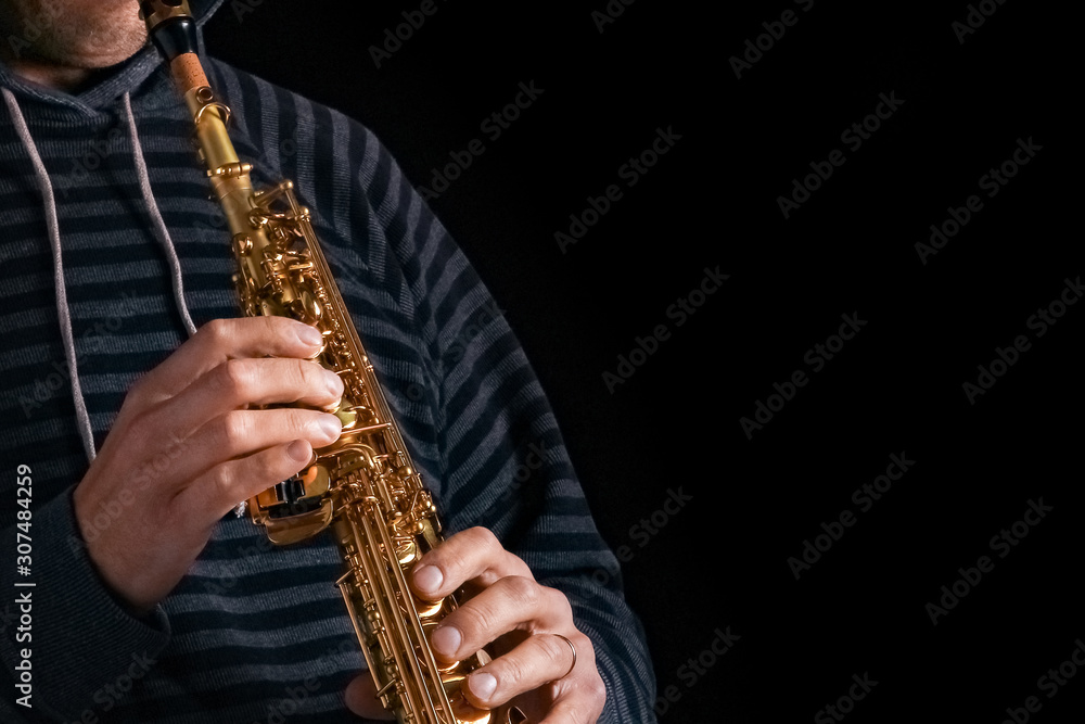 Naklejka premium soprano saxophone in the hands of a guy on a black background