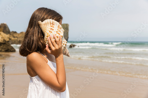 A young girl listening to a conch shell on a beach