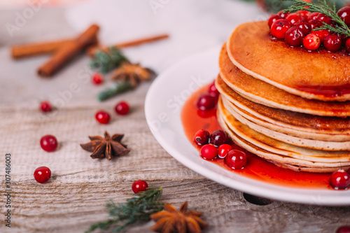 Stack of american pancakes with fresh cranberry and jam in white plate on wooden rustic table decorated Christmas tree, delicious dessert for breakfast in winter, vintage style. 