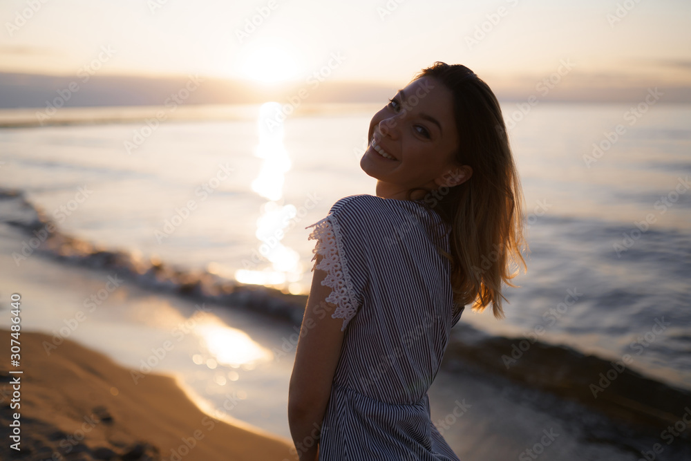 Medium shot: Portrait of a Beautiful blonde woman in a light blue dress on the Baltic Sea beach during sunset with vivid colors Medium shot: Portrait of a Beautiful blonde woman in a light blue dress on the Baltic Sea beach during sunset with vivid colors