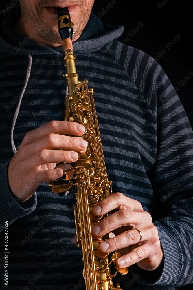 Naklejka premium soprano saxophone in the hands of a guy on a black background