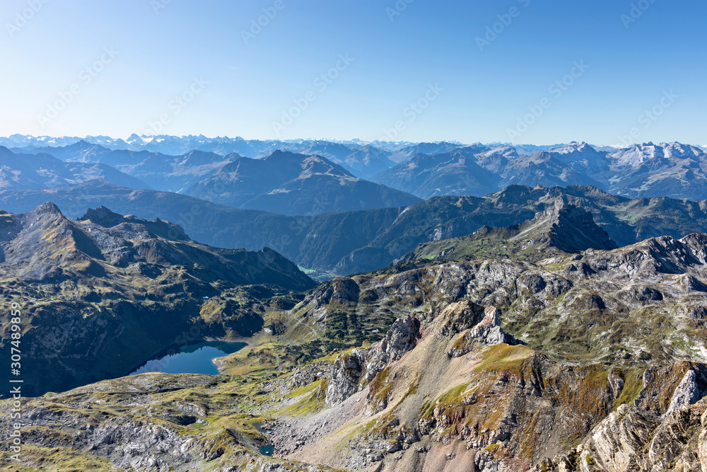 View from the summit of Rote Wand mountain (Vorarlberg, Austria). Wild alpine landscape with rocky mountains, forest and a lake under blue sky.