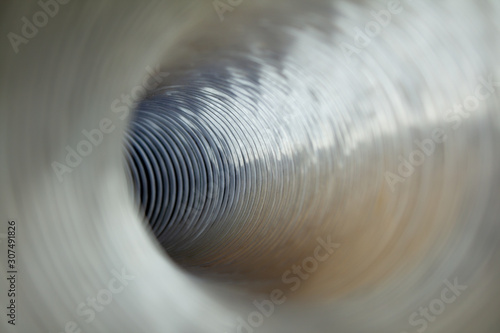 Optical illusion of photo. Futuristic plastic pipe inside iridescent swirling spiral. Bright highlights and large depth of field. Abstract lights and textures for design. Golden shades.