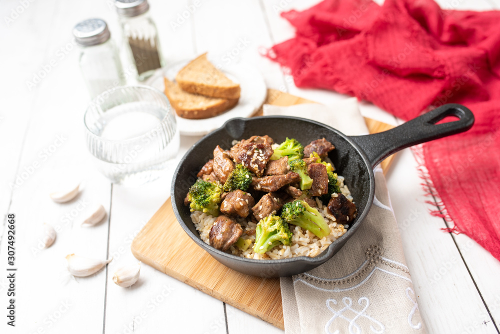 Beef and broccoli over rice in a black skillet topped with sesame seeds Beef and broccoli over rice in a black skillet topped with sesame seeds