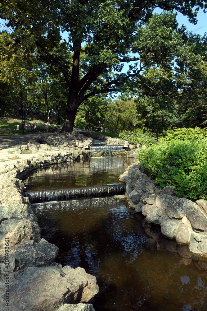 Water cascade in the city park Bastion Hill in Riga center with shadows under trees on sunny day