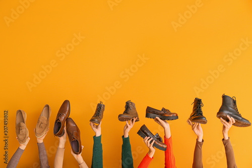 Many hands with different stylish shoes on color background