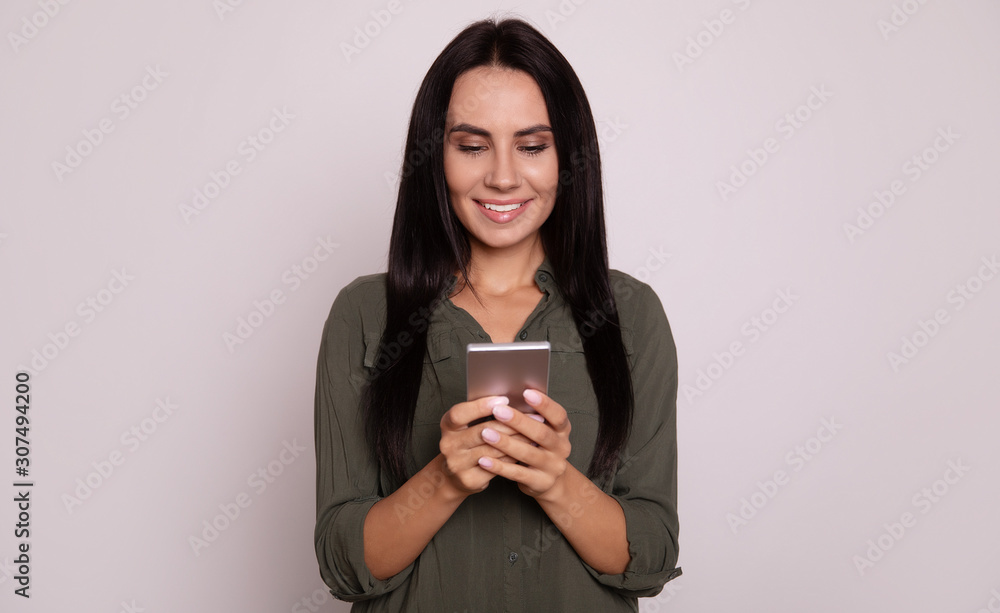 Communication. Close-up photo of a good-looking woman with long hair, who is browsing the Internet and smiling while reading something on the phone. Communication. Close-up photo of a good-looking woman with long hair, who is browsing the Internet and smiling while reading something on the phone.
