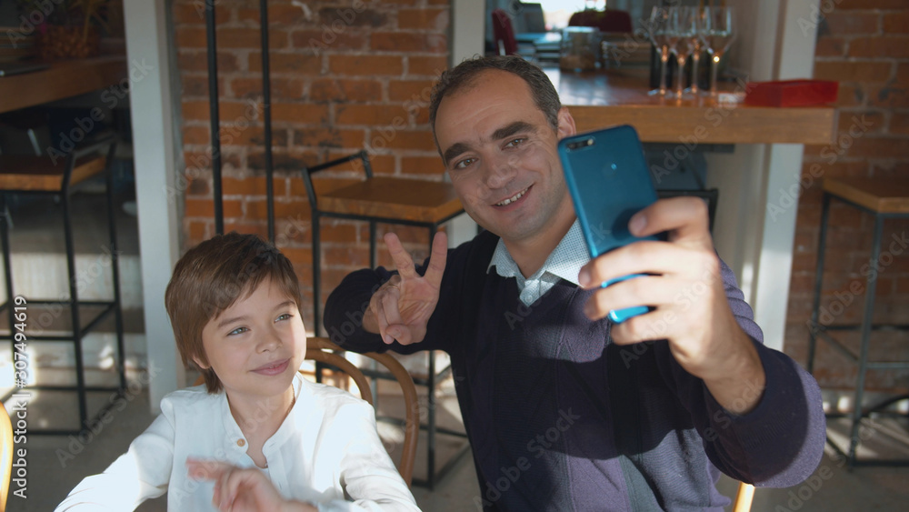 Father and son take selfie on the phone in cafe