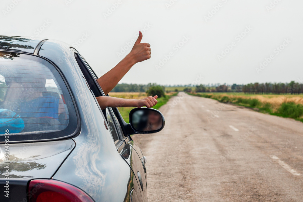 Happy traveler with thumbs up. People on the road concept. Woman showing thumbs up from car window with sunset sky at background