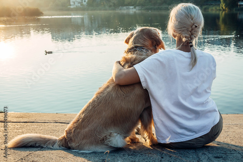 Blonde girl with dog from the back , lake view .