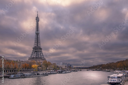 Paris, France - November 24, 2019: The Eiffel tower from embankment at the river Seine in Paris. Ship and boats on river at cloudy day