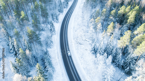 White car drives empty road in forest in the cold Finnish winter. Tourists on road trip cruising through the idyllic snow covered countryside and woods. © raland