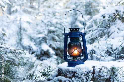  Lantern standing and glowing in the snow at evening. Vintage hand lantern a wooden stump in the woods during the winter season. Christmas theme. Winter background. © raland