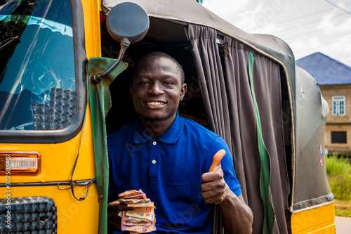 young african man driving a rickshaw taxi counting his money smiling giving a thumbs up photo