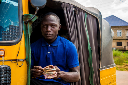 young african man driving a rickshaw taxi counting his money smiling photo