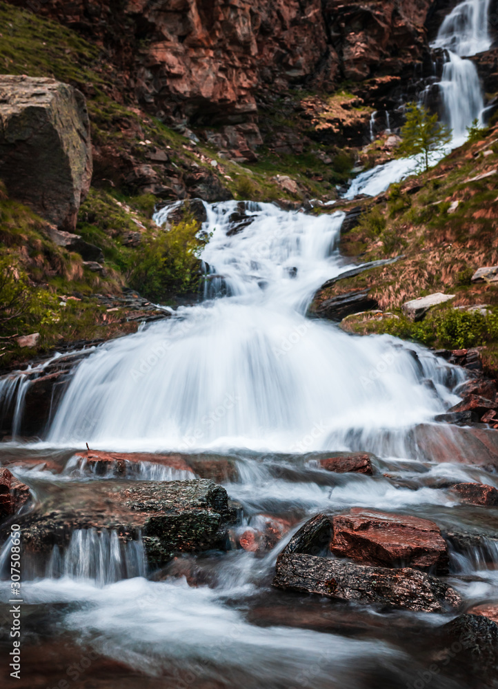 Waterfall in Gran Paradiso Italian alps mountains in Graian Alps in Piedmont, Italy with snow capped peaks. Waterfall in Gran Paradiso Italian alps mountains in Graian Alps in Piedmont, Italy with snow capped peaks.