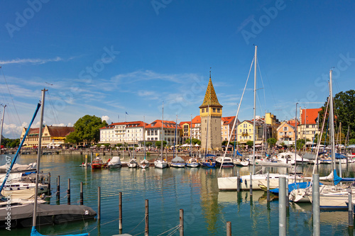 Boats moored at harbor with buildings in background against blue sky, Lindau, Germany