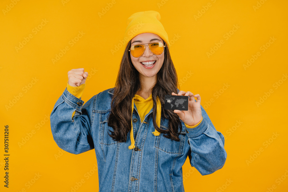Young asian girl showing credit card isolated over yellow background Young asian girl showing credit card isolated over yellow background