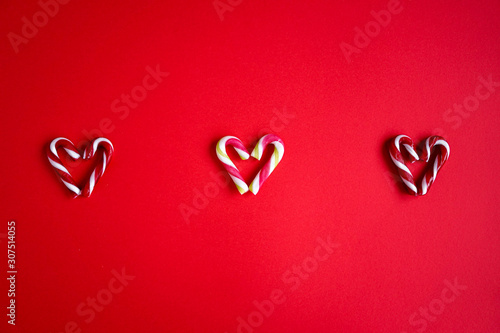Red and green candy canes on red background. Hearts made out of sugar candy canes. Christmas, holiday concept