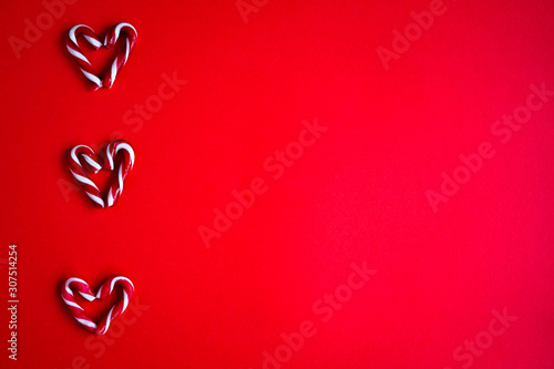 Candy canes shaped as hearts on red background. Christmas flatlay composition with copy space