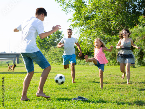 Group of smiling children and parents having fun together outdoors playing football