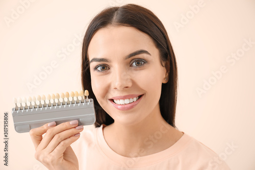 Beautiful young woman with teeth color samples on light background