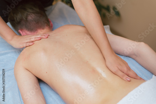 Woman massages under the shoulder blade on the back. Masseur does massage to a man lying on a couch