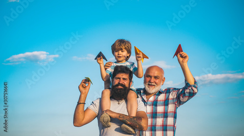 Young boy with father and grandfather enjoying together in park on blue sky background. Fathers day - grandfather, father and son are hugging and having fun together. © Volodymyr