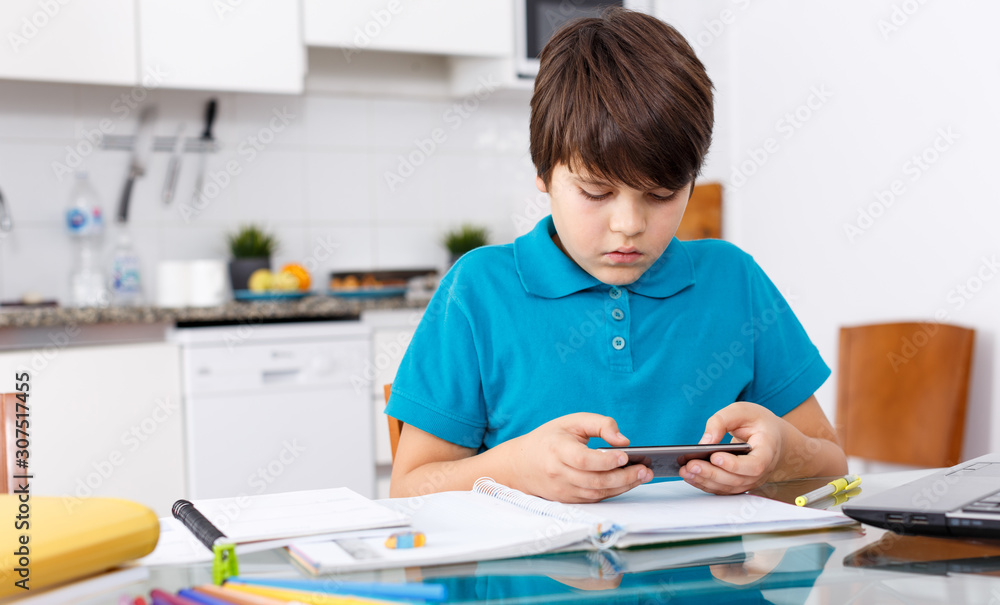 Naklejka premium Boy using phone while doing homework