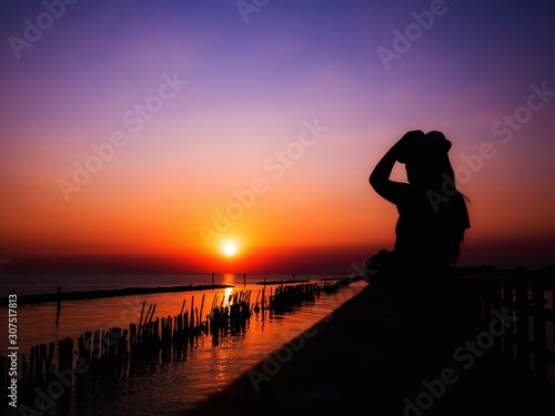 A woman silhouette standing Selfie on wooden pier at the sea with beautiful cloudy sunset.