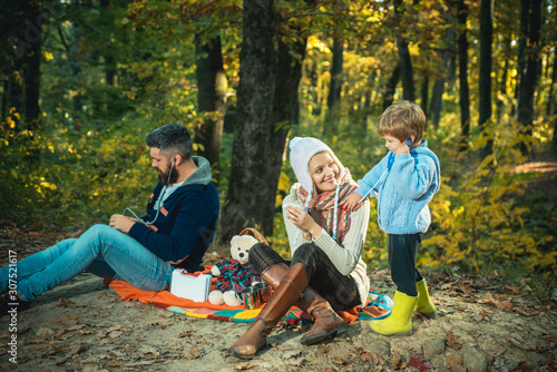 Happy young family walking at beautiful fall autumn nature. Mother wearing a ear-flapped hat and plaing with her son a doctor game. Little cute boy is smiling. Family concept.