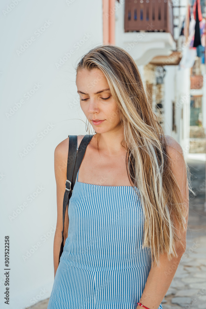 Fototapeta premium Young beautiful woman in blue dress posing on a narrow street at Nisyros island, Greece.