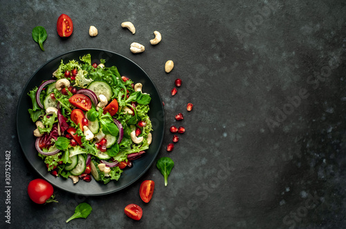 Salad with pomegranate, tomatoes, fresh cucumbers, onions, sesame seeds and cashew nuts, spices on a stone background. Healthy vegetarian food. with copy space for your text