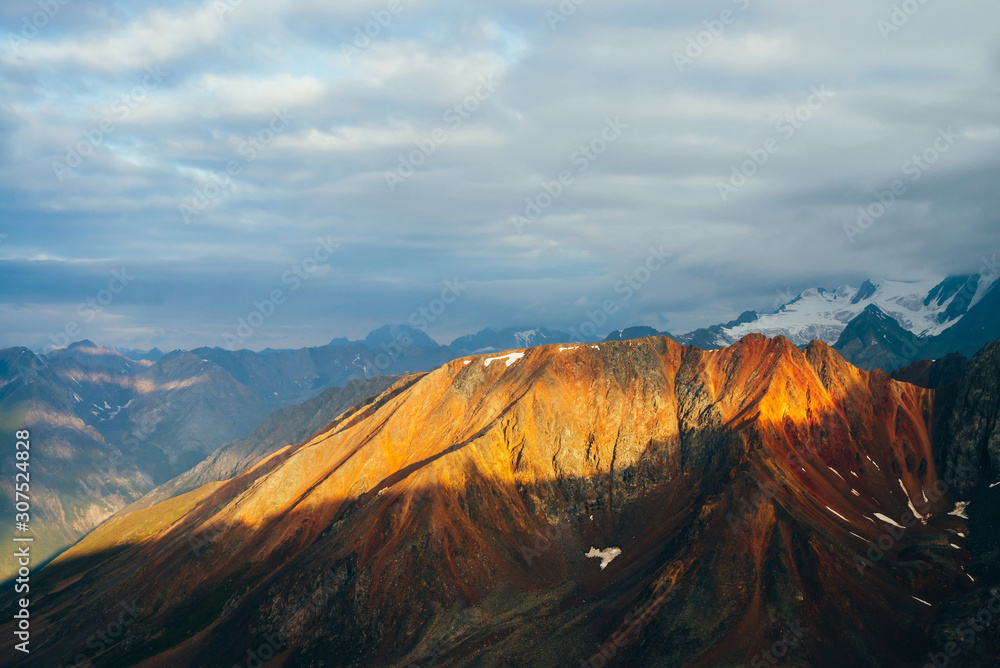 Atmospheric alpine landscape with red rockies in golden hour. Scenic view to big orange rocks and giant snowy mountains with glacier in sunrise. Wonderful highland scenery. Flying over mountains.
