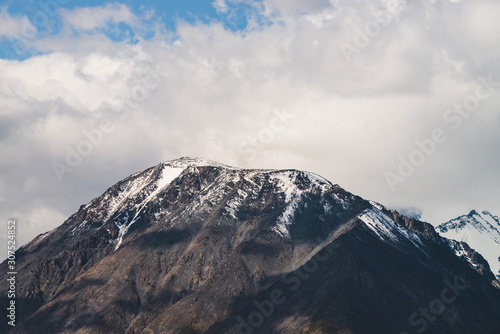 Atmospheric alpine landscape to snowy mountain ridge in sunny day. Snow shines in day light on mountain peak. Beautiful shiny snowy top. Wonderful scenery to low clouds above range covered with snow. © Daniil