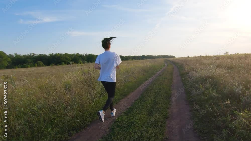 Young fitness sport woman running on road at sunset. Athlete runner feet running on road, slow motion. Young fitness sport woman running on road at sunset. Athlete runner feet running on road, slow motion.