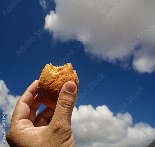 Holding a COXINHA DE FRANGO and having blue sky with cloud as background. The COXINHA DE FRANGO is a very popular food in Brazil. photo