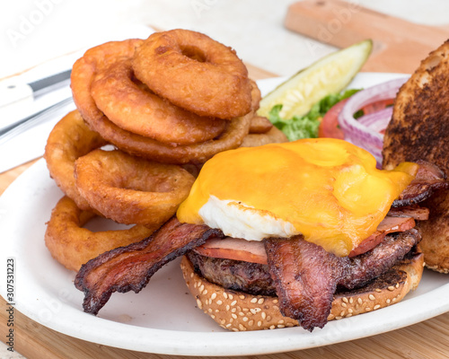 Bacon cheeseburger topped with ham and a fried egg. Served with onion rings and a pickle.