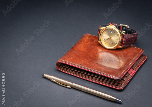 Brown leather wallet with watch and gold pen isolated on black gradient background. Luxury accessories. Gift concept for men. 