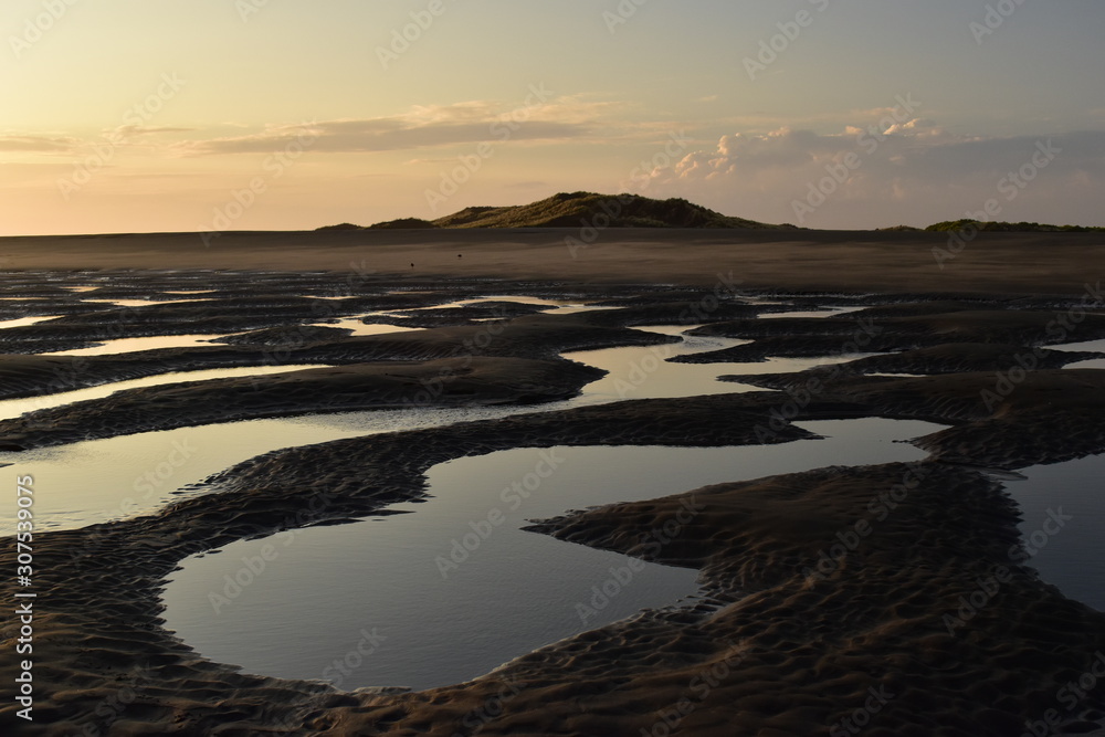 A small puddles in the sand after low tide in sunset light
