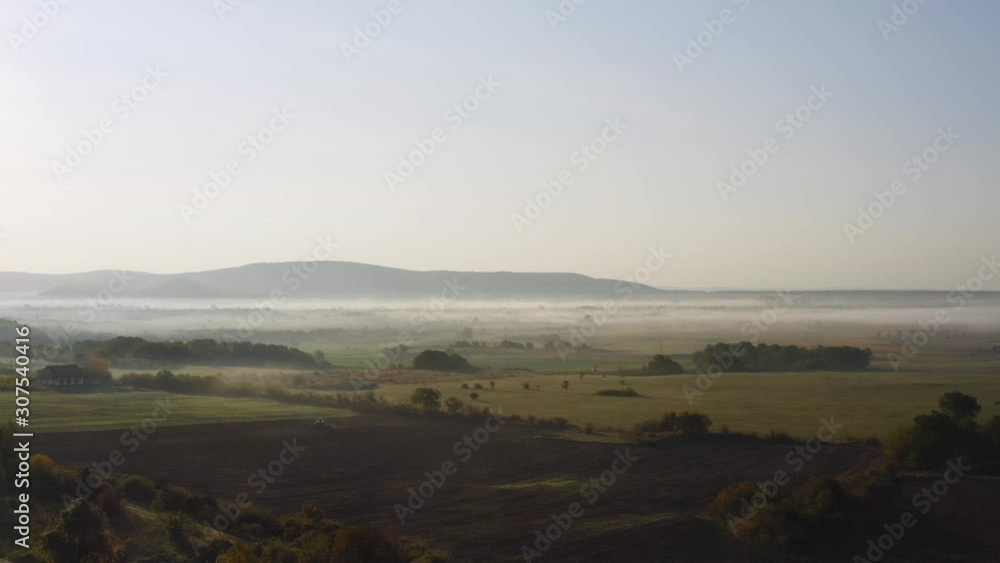 Foggy morning drone shot over the field with tractor and trees. Foggy morning drone shot over the field with tractor and trees.