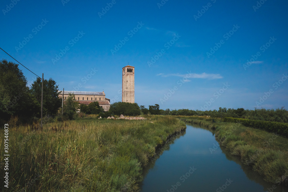 Cathedral of Santa Maria Assunta and bell tower by river on island of Torcello, Venice, Italy