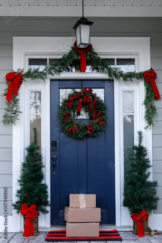 Navy blue front door of contemporary new construction siding gray home decorated for Christmas holidays with wreath trees and garland with packages and boxes shipped from e-commerce online shopping